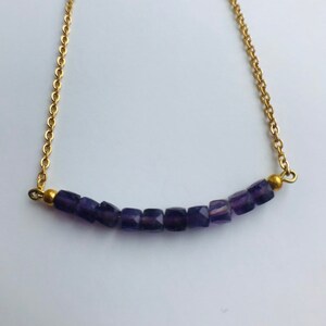 May include: A gold chain necklace with a row of small, square-shaped amethyst beads.