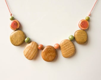 Puede incluir: Un collar de cuentas de madera con un esquema de color rosa y verde. El collar presenta cuentas redondas de madera con un acabado de madera natural y cuentas redondas más pequeñas en rosa y verde.