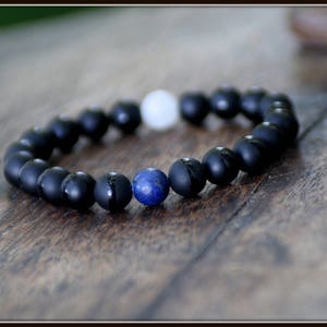 Op de afbeelding: Een zwarte kralen armband met een enkele blauwe edelsteenkralen. De armband is gemaakt van matte zwarte kralen en heeft een eenvoudig ontwerp.