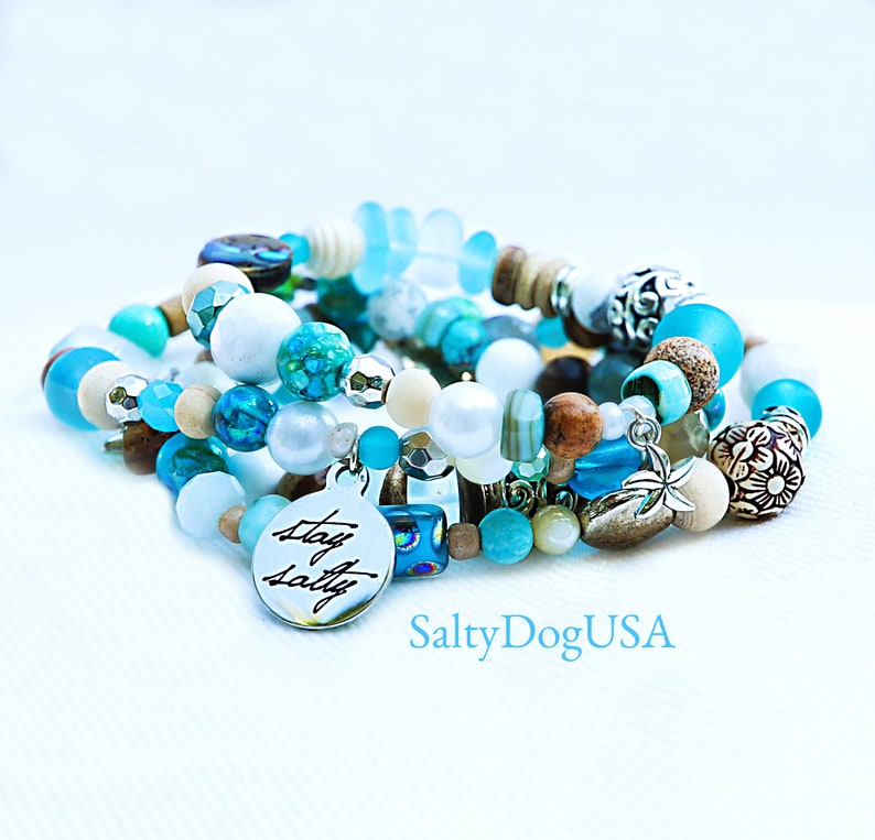 May include: A set of five bracelets featuring a mix of blue, white, and brown beads. The bracelets have a charm that says "Stay Salty".