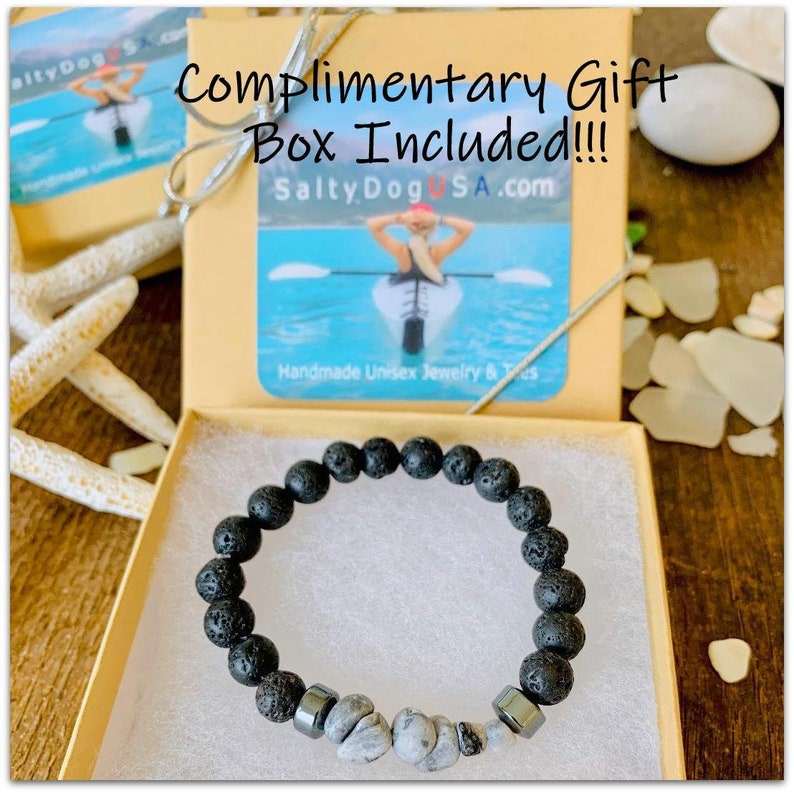 Op de afbeelding: Een zwarte armband van lavasteen met grijze en zilveren kralen. De armband zit in een kleine, bruine geschenkdoos met een witte achtergrond en de tekst "Complimentary Gift Box Included!!! SaltyDogUSA.com Handmade Unisex Jewelry & Tes" erop gedrukt.