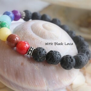 May include: A rainbow chakra bracelet with black lava beads and silver spacers. The bracelet is on a seashell. "With Black Lava" is written on the shell.