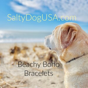 May include: A yellow Labrador Retriever dog sits on a sandy beach, looking out at the ocean. The text "SaltyDogUSA.com" is at the top of the image, and the text "Beachy Boho Bracelets" is at the bottom of the image.