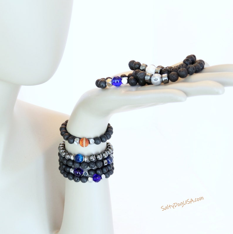 Op de afbeelding: Een set van vijf armbanden met zwarte lavastenen, zilveren kralen en kleurrijke accentkralen. De armbanden zijn gestapeld op de arm van een mannequin. De tekst "SaltyDogUSA.com" is zichtbaar in de rechterbenedenhoek van de afbeelding.