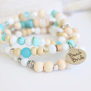 May include: A multi-strand bracelet with wooden beads, turquoise beads, and a silver charm that says "Beach Bride".