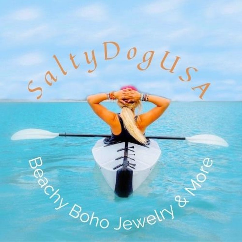 May include: A woman in a kayak on a calm blue ocean with a sky blue sky. The text "Salty Dog USA" is in a circle above the woman. The text "Beachy Boho Jewelry & More" is in a circle below the woman.