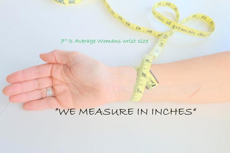May include: A yellow measuring tape wrapped around a person's wrist. The tape reads "7" inches, which is the average woman's wrist size. The text "WE MEASURE IN INCHES" is written below the wrist.
