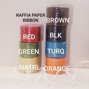 May include: Assortment of raffia paper ribbon rolls in various colors, including brown, black, red, green, turquoise, and orange. The text "Raffia Paper Ribbon" is printed on the image.