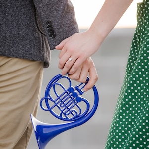 Puede incluir: Una pareja tomados de la mano mientras sostienen un cuerno franc&eacute;s de juguete azul.