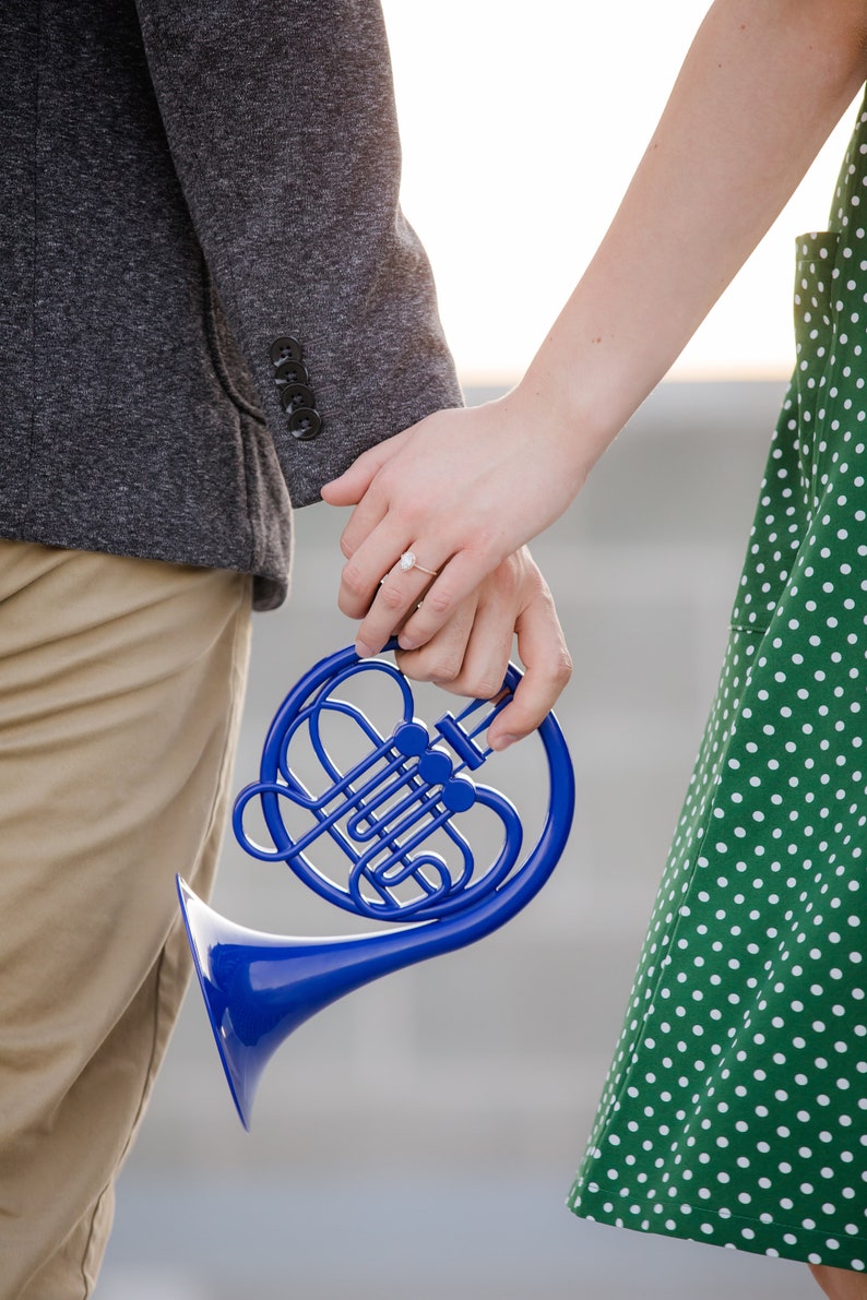 Puede incluir: Una pareja tomados de la mano mientras sostienen un cuerno franc&eacute;s de juguete azul.