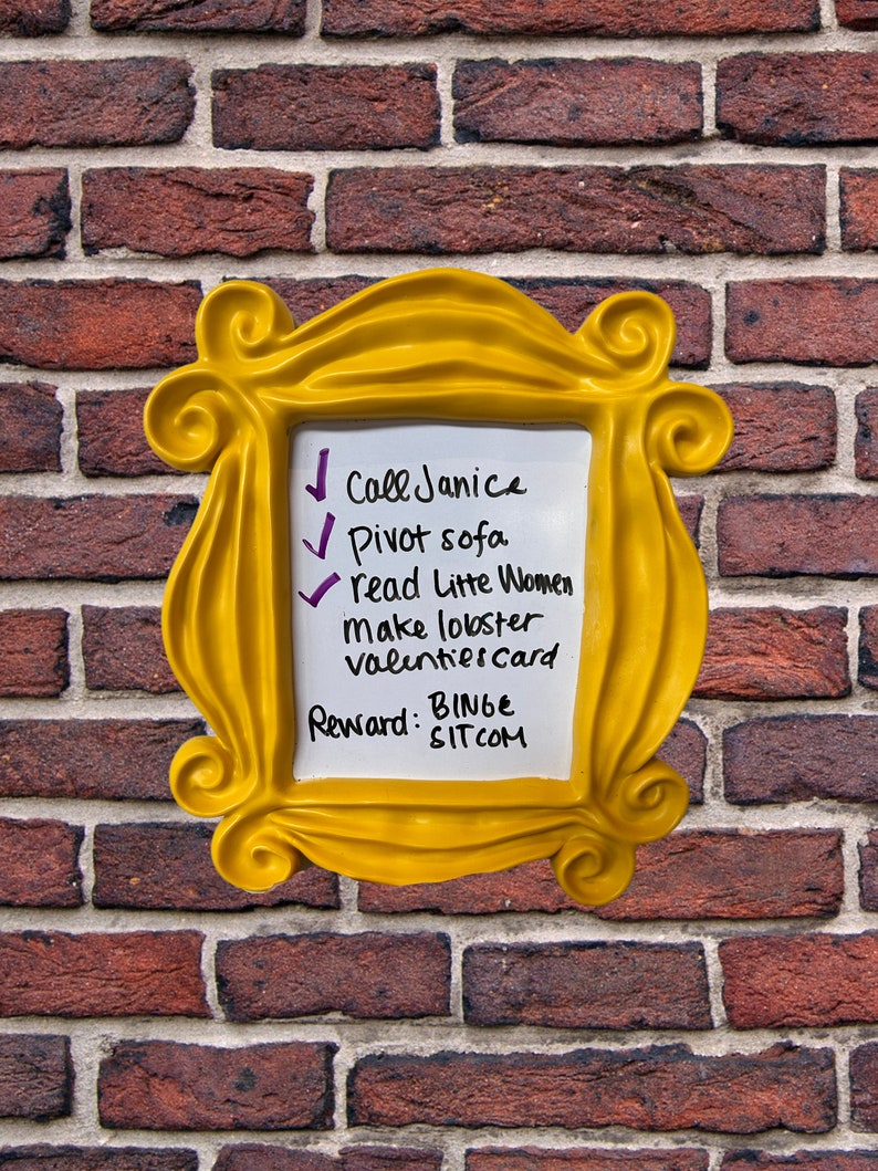 Pu&ograve; includere: Una cornice gialla con una lavagna bianca cancellabile a secco all'interno. La lavagna ha un elenco di compiti scritti su di essa, tra cui "Chiama Janice", "Gira il divano", "Leggi Piccole donne", "Fai l'aragosta", "Biglietto di San Valentino" e "Ricompensa: Binge Sitcom".