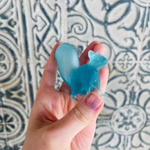 May include: A light blue glass squirrel figurine. The squirrel is standing on its hind legs with its tail curled up behind it.