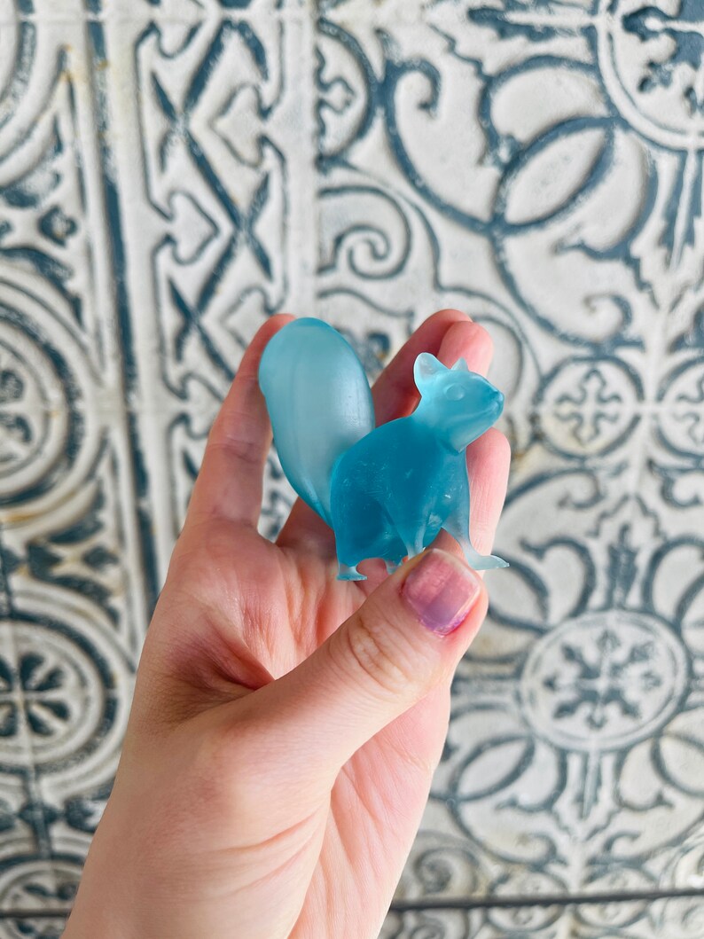 May include: A light blue glass squirrel figurine. The squirrel is standing on its hind legs with its tail curled up behind it.