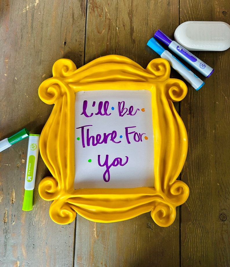 Pu&ograve; includere: Una cornice gialla con una lavagna bianca cancellabile a secco all'interno. La lavagna ha le parole "I'll be there for you" scritte con un pennarello viola. Ci sono anche tre pennarelli cancellabili a secco sul tavolo, uno verde, uno blu e uno viola.