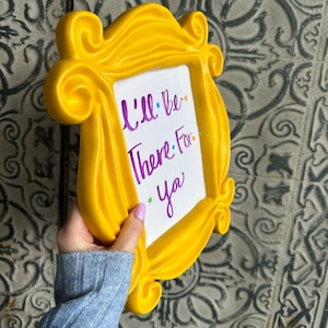 Pu&ograve; includere: Cornice in plastica gialla con un inserto di lavagna bianca cancellabile a secco. La lavagna ha una scritta viola che dice "Sar&ograve; l&igrave; per te."