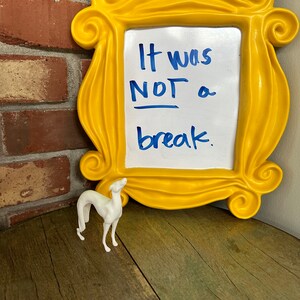 Pu&ograve; includere: Una cornice gialla con una lavagna bianca cancellabile a secco che dice "It was NOT a break." Una statuetta bianca di un cane &egrave; in primo piano.
