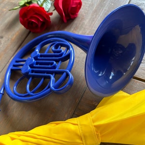 Puede incluir: Un cuerno franc&eacute;s de juguete de pl&aacute;stico azul con un fondo de tela amarillo.