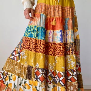 Può includere: Una gonna lunga a balze con un design patchwork caratterizzato da vari motivi, tra cui stampa leopardata, disegni floreali, forme geometriche e una stampa di limoni su sfondo bianco. La gonna presenta un elastico in vita con coulisse.