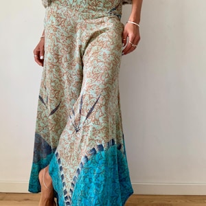 Può includere: Un paio di pantaloni a gamba larga con una stampa floreale in tonalità di marrone, blu e verde. I pantaloni hanno un orlo ampio e fluido e una vita aderente.
