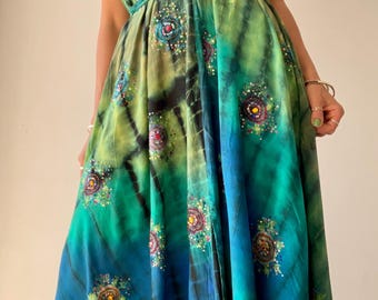 May include: A flowing, tie-dye maxi dress in shades of green and blue. The halter-style dress features a V-neck and is cinched at the waist with a thin, green belt. The dress is adorned with embroidered floral accents.