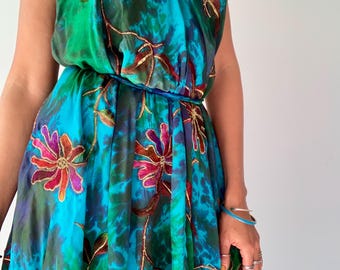 May include: A sleeveless halter-neck dress featuring a vibrant tie-dye pattern in shades of turquoise, emerald green, and deep blue. The fabric is adorned with embroidered floral motifs in magenta, orange, and brown with metallic gold outlines.
