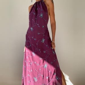 Könnte beinhalten: Ein langes, violettes Halfterkleid mit Blumenmuster und Pailletten. Das Kleid hat einen Schlitz an der Seite und einen Halfterausschnitt.
