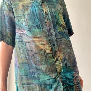 May include: A short-sleeved button-down shirt with an abstract geometric pattern in shades of green, brown, and blue.