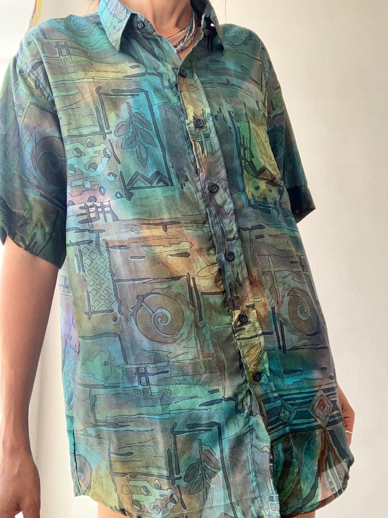 May include: A short-sleeved button-down shirt with an abstract geometric pattern in shades of green, brown, and blue.