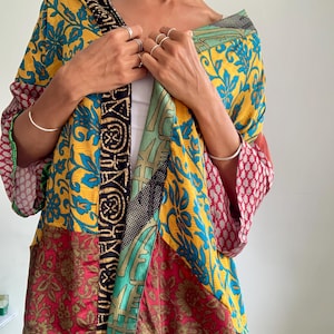 Könnte beinhalten: Eine locker sitzende Jacke im Kimono-Stil mit einem lebendigen Patchwork-Design. Das Kleidungsstück zeigt eine Mischung aus gelben, türkisfarbenen, roten und schwarzen Stoffbahnen mit verschiedenen Blumen- und geometrischen Mustern sowie einer markanten schwarz-goldenen Borte.
