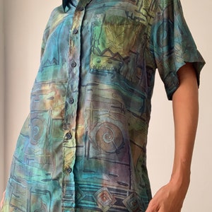 May include: A short-sleeved button-down shirt with an abstract, geometric print in shades of blue, green, brown, and beige.