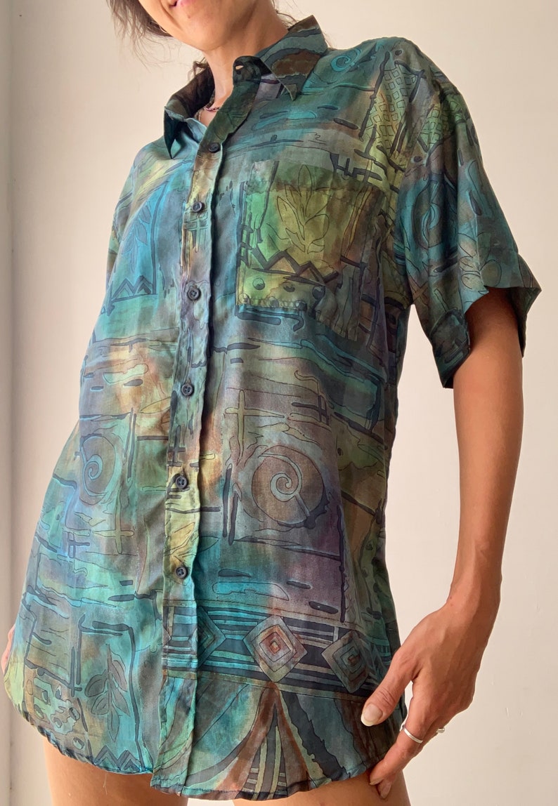 May include: A short-sleeved button-down shirt with an abstract, geometric print in shades of blue, green, brown, and beige.