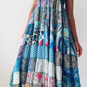 Op de afbeelding: Een strapless maxi-jurk met een patchwork-ontwerp. De jurk heeft een smocked lijfje in zeegroen en een rok bestaande uit verschillende panelen met patronen in tinten blauw, zeegroen, roze en wit. De jurk heeft een gelaagde constructie.