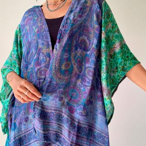 May include: A blue, purple, and green paisley print kimono with an open front. The sleeves are a contrasting green with a delicate pattern. The kimono has a V-neck and a loose, flowing design. The fabric is lightweight and appears to drape well.