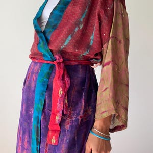 May include: A colorful wrap dress with a tie waist. The dress features a mix of colors, including red, purple, blue, and green. The sleeves are long and flowing, and the dress is made of a lightweight fabric.