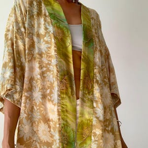 Könnte beinhalten: Ein beiger Seidenkimono mit floralem Muster und grünen und gelben Akzenten. Der Kimono hat einen weiten, offenen Kragen und lange Ärmel.