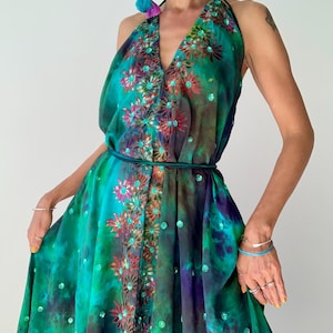 May include: A teal, green, and purple halter-neck dress with floral embroidery and sequin details. The dress has a V-neck and a flowing skirt, with a matching belt at the waist. The dress is a bohemian style, perfect for a summer occasion.