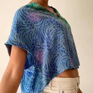 May include: A blue and green patterned top with a V-neck design. The top features a floral and swirl pattern in shades of blue and pink. The top is a cropped style.
