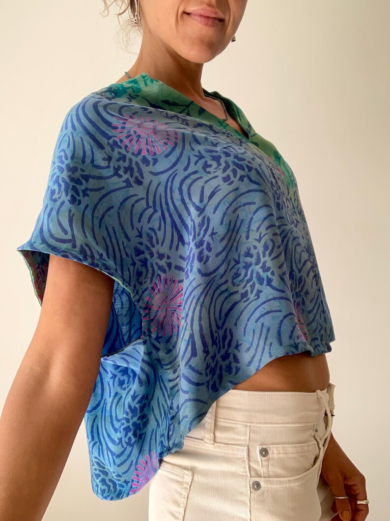 May include: A blue and green patterned top with a V-neck design. The top features a floral and swirl pattern in shades of blue and pink. The top is a cropped style.