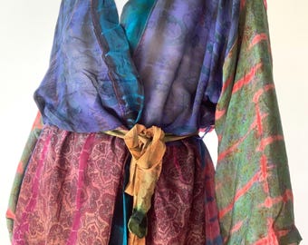 May include: A colorful, patterned kimono-style wrap with a tie belt. The wrap features shades of purple, blue, green, and pink. The fabric has a silky appearance and a paisley design. The tie belt is a mix of gold and green.