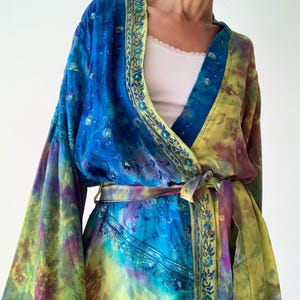 Könnte beinhalten: Ein lebendiger Kimono-Bademantel im Batik-Design in Blau-, Grün- und Lilatönen. Der Bademantel hat aufwendige Stickereien an den Rändern und einen passenden Bindegürtel. Die Ärmel sind weit und fließend.