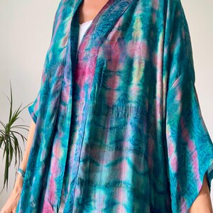 May include: A loose-fitting kimono-style jacket featuring a vibrant tie-dye pattern in shades of teal, turquoise, and magenta. The garment has wide, flowing sleeves, an open front design, and a lightweight, semi-sheer fabric texture throughout.