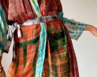 May include: A colorful kimono-style robe with a tie-waist. The robe features a mix of patterns and colors, including orange, green, blue, and brown. The sleeves have a tie-dye effect. The robe is made of a lightweight fabric.