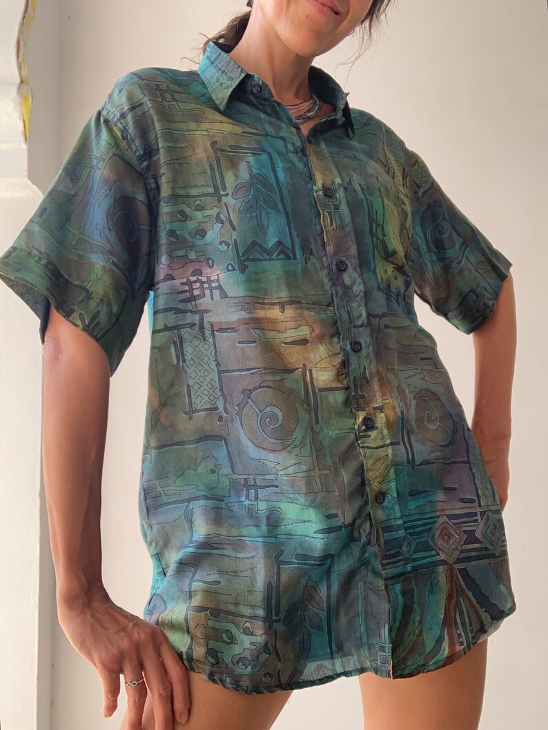 May include: A short-sleeved button-down shirt with an abstract geometric pattern in shades of green, blue, and brown.