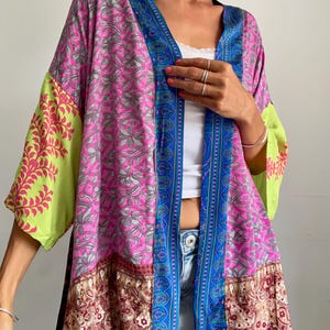 Può includere: Una giacca in stile kimono dal taglio ampio con un vivace design patchwork. Il capo presenta pannelli rosa acceso con motivi floreali grigi, maniche verde lime con motivi a foglie rosse e un orlo paisley marrone scuro con bordo blu.