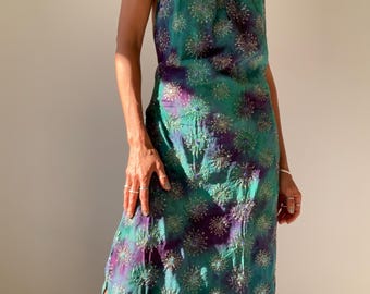 May include: A long, flowing halter dress with a tie-dye pattern in shades of teal, purple, and blue. The dress is adorned with silver and purple sequins in a starburst design.