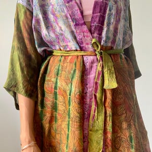 May include: A colorful silk kimono with a tie belt. The kimono is made of different fabrics with a patchwork design. The kimono is green, purple, orange, and pink.