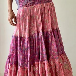 May include: A pink and purple tiered skirt with a floral print. The skirt has a gathered elastic waistband and a flowing silhouette.