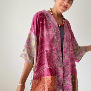 Op de afbeelding: Een roze en oranje zijden kimono met een bloemenpatroon. De kimono is gemaakt van verschillende stukken stof die aan elkaar zijn genaaid.