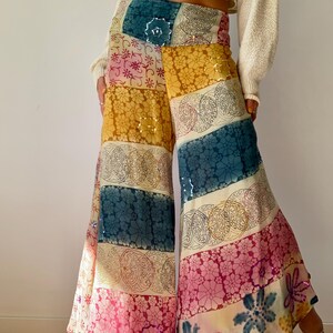 Puede incluir: Pantalones palazzo de patchwork coloridos con estampados florales y geométricos en tonos amarillos, rosas, turquesas y crema. Los pantalones de pernera ancha tienen adornos de lentejuelas y cintura alta. Los pantalones son de tejido ligero.