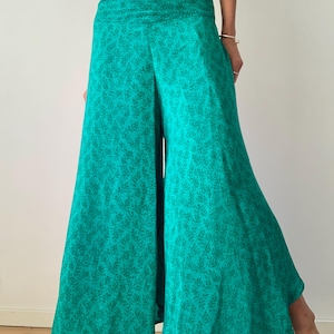 May include: Wide-leg teal pants with a subtle leaf pattern. The pants have a high, folded waistband and a flowing silhouette. The fabric appears lightweight and comfortable, suitable for casual wear. The pants are a vibrant shade of teal.